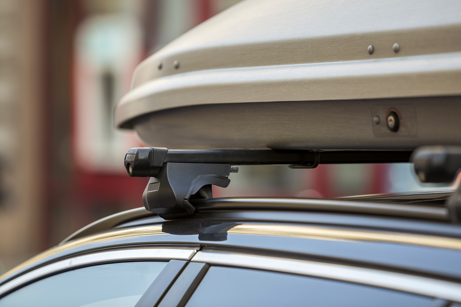 Nahaufnahme der beigen Dachbox, die auf dem schwarzen Dachträger montiert ist, welcher auf einer integrierten Schiene sitzt.